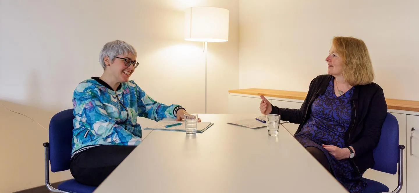 zwei Frauen sitzen im Gespräch an einem hellen Tisch 