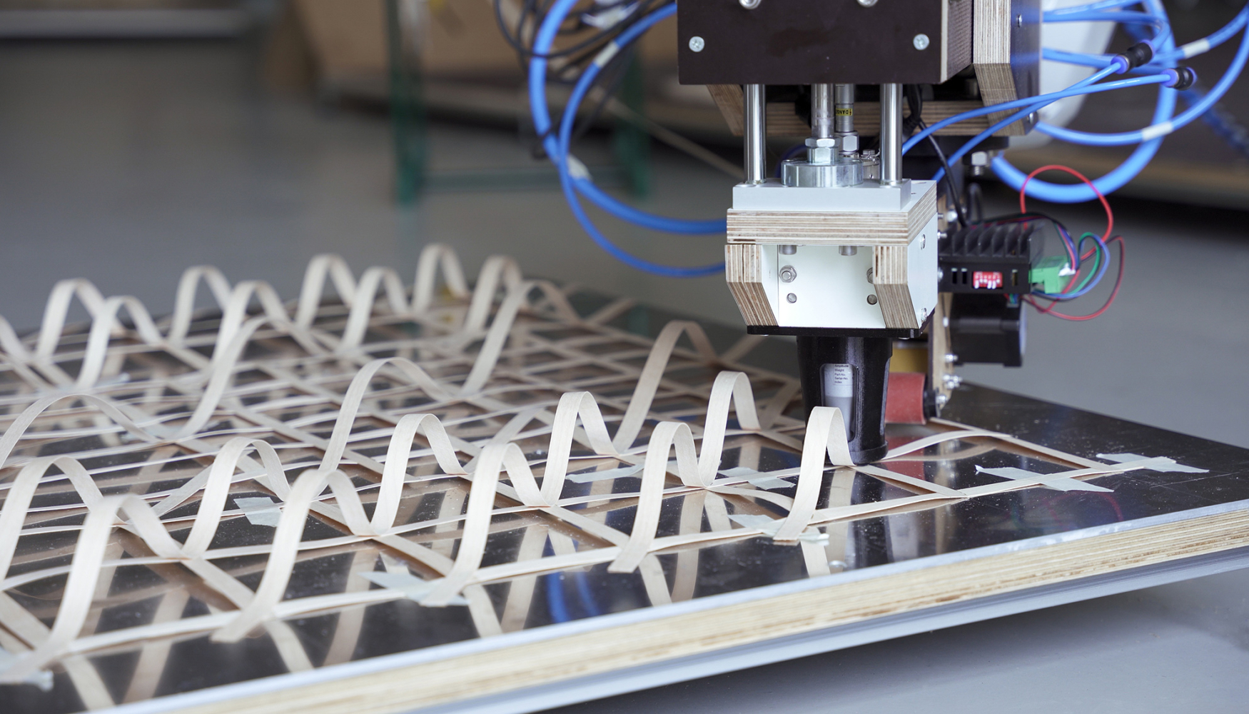 Nachaufnahme von einem Roboter, der dünne Holzstreifen auf einer Platte in einem geometrischen Muster verschweißt.