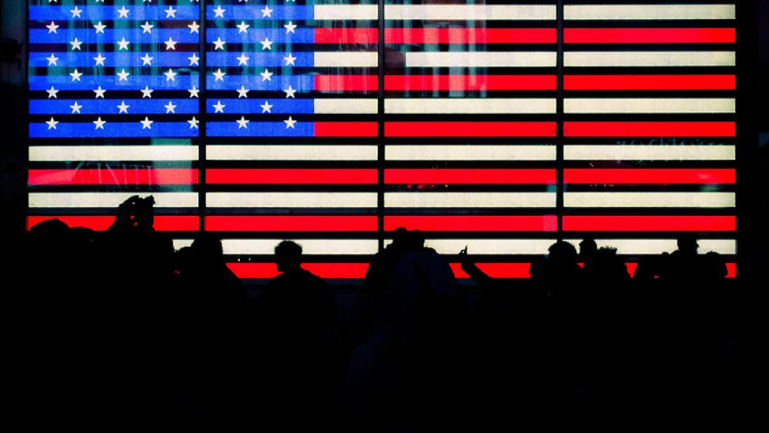 Die Flagge der USA ist zu sehen, eingerahmt im Vordergrund durch Umrisse von Personen.
